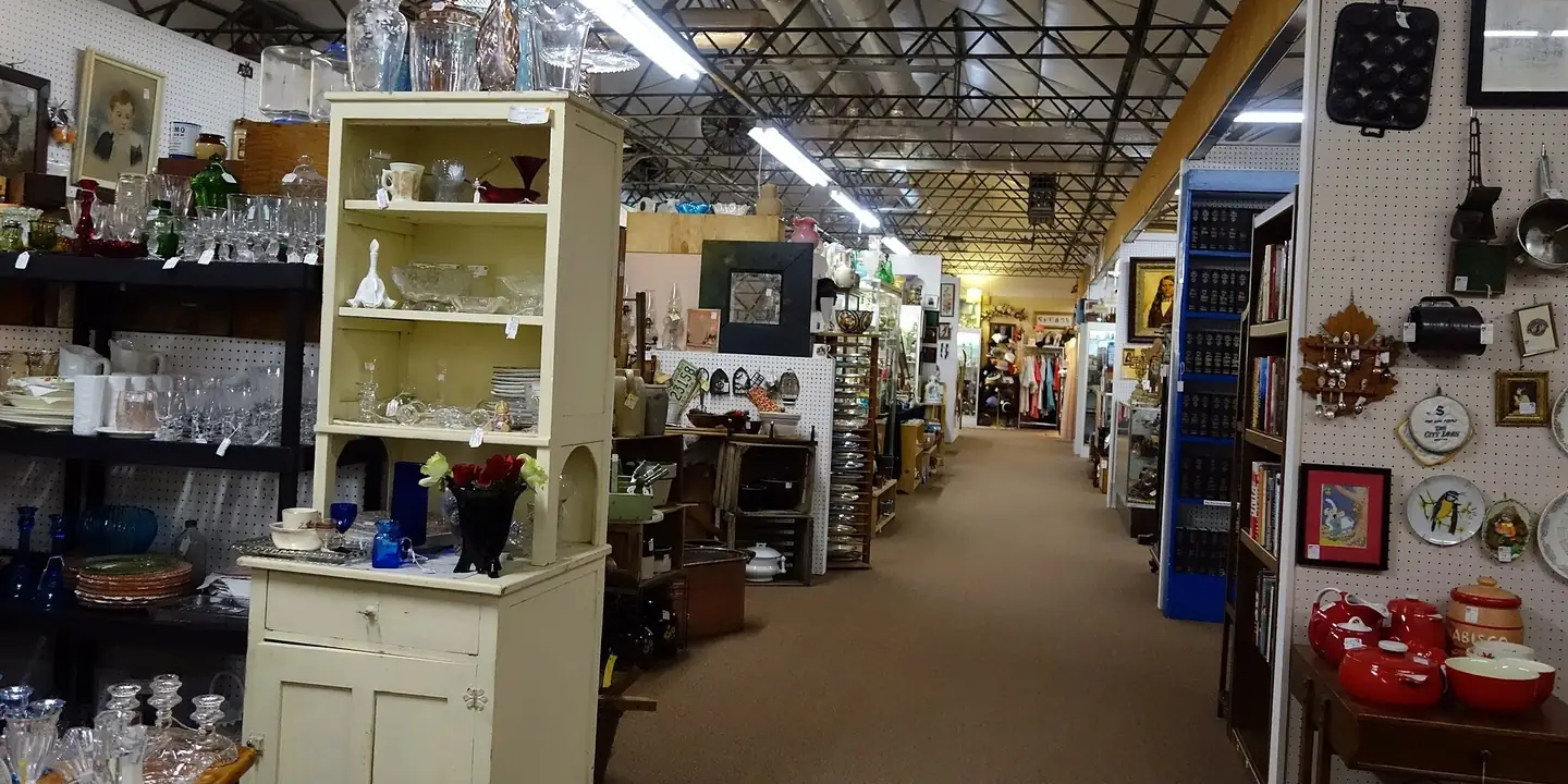 Long aisle of dealer booths with glassware and cabinets in an antique mall