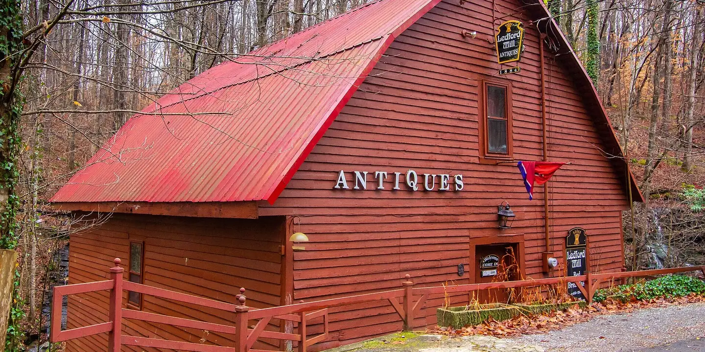 Red wooden mill building with ANTIQUES lettering in the woods